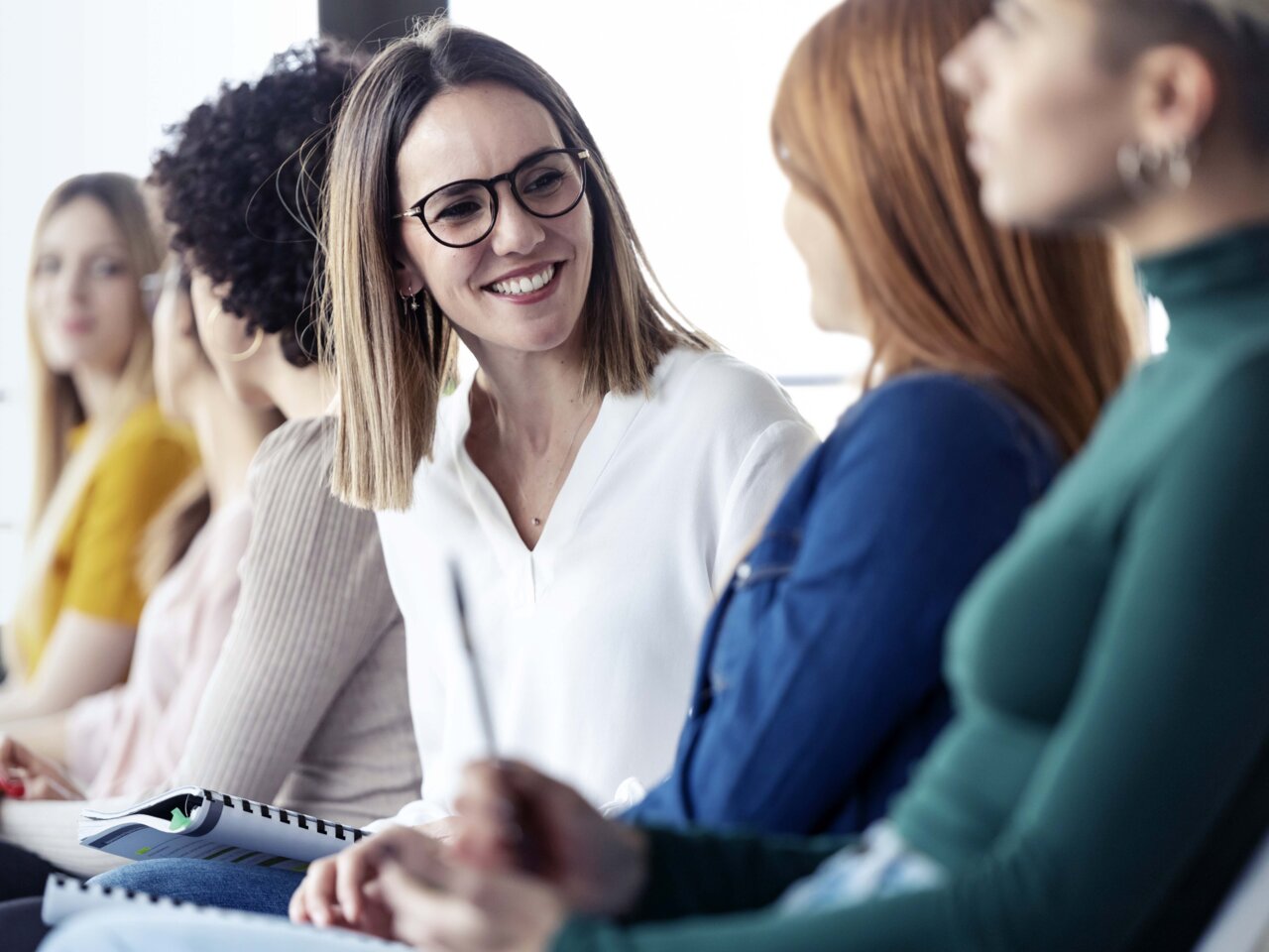 Women sitting in a row of chairs talking to each other Women sitting in a row of chairs talking to each other