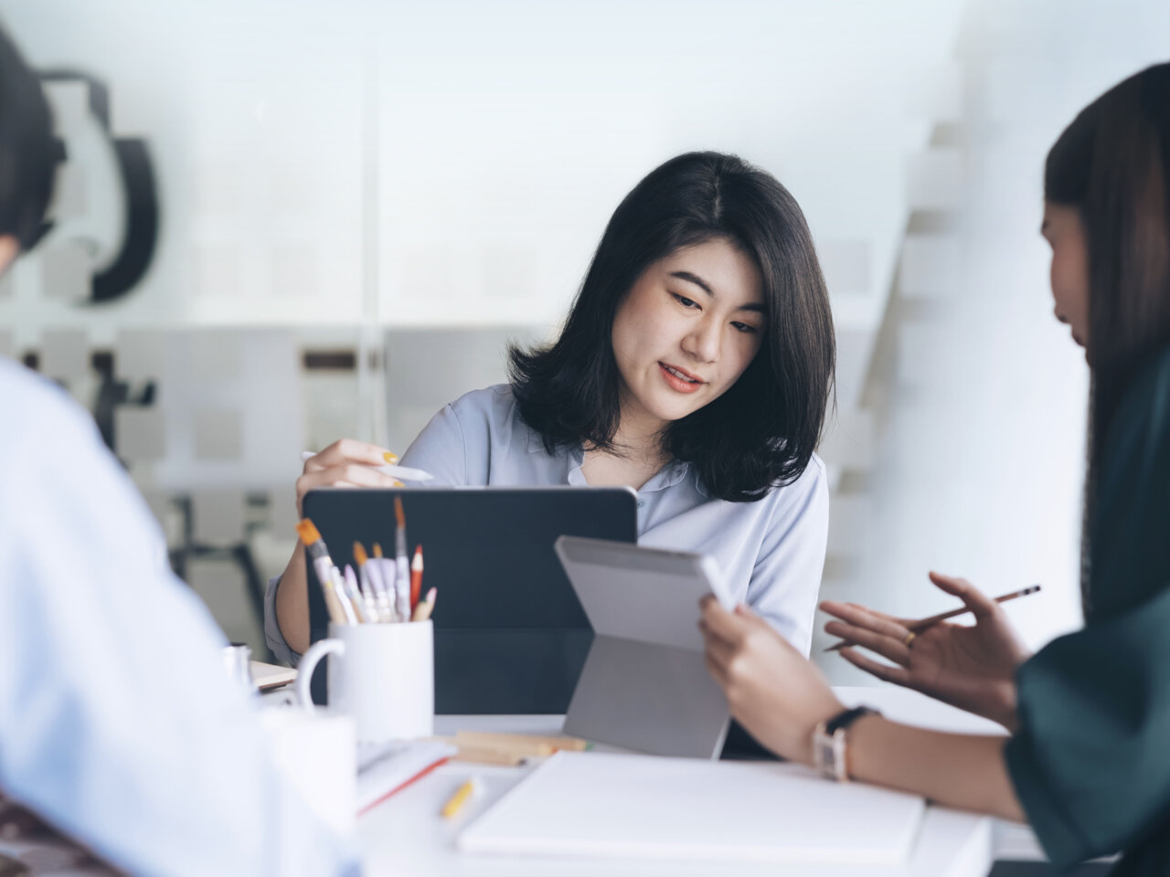 Women sitting a desk look at each others laptops Women sitting a desk look at each others laptops